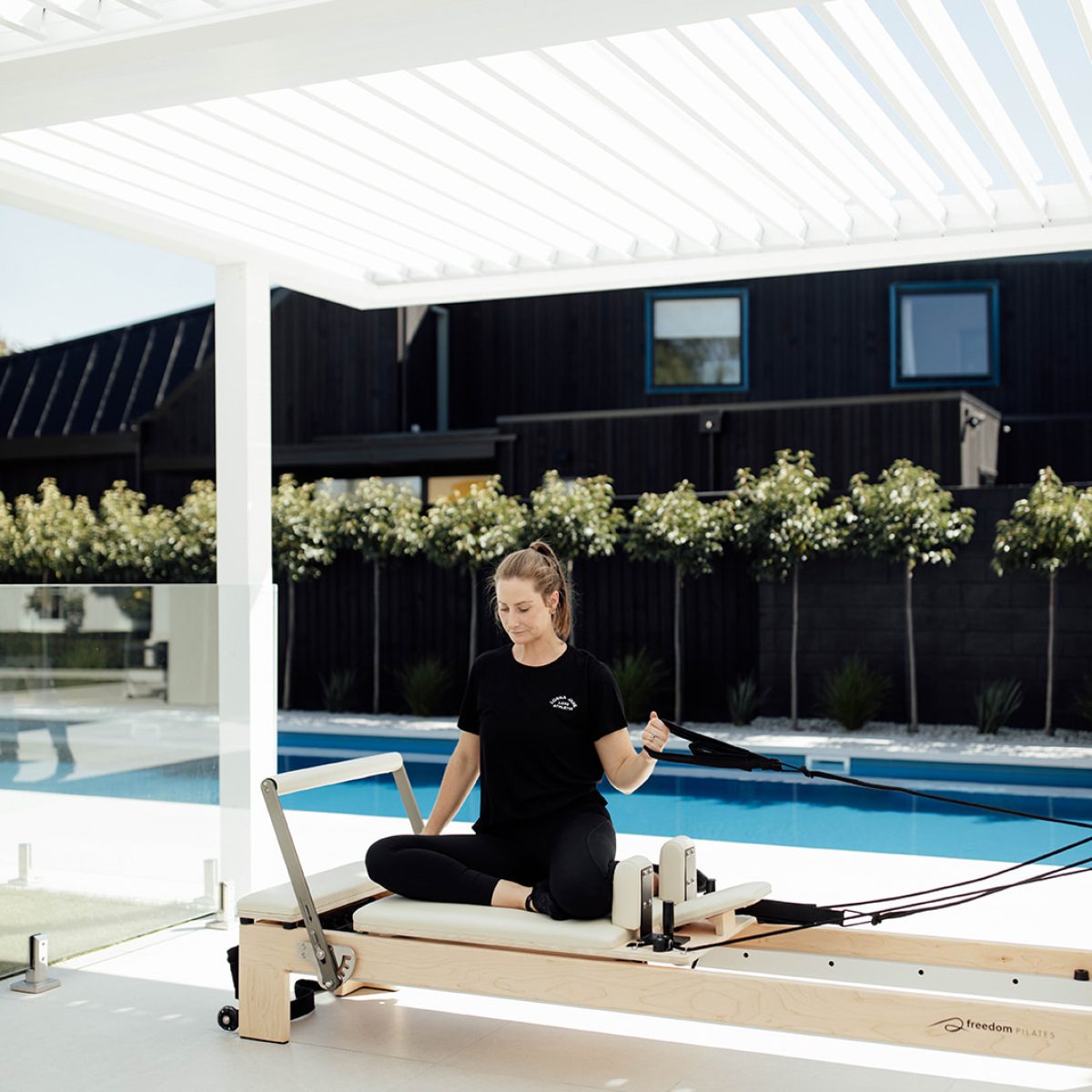 A young woman using her Freedom Pilates reformer on her patio
